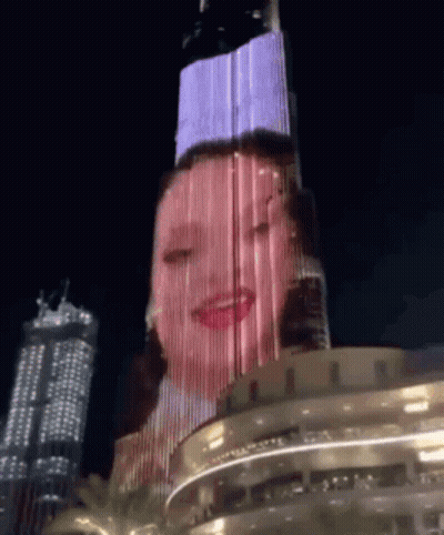 A Woman 'S Face Is Projected On A Building At Night GIF