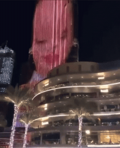 A Woman 'S Face Is Projected Onto The Side Of A Building GIF