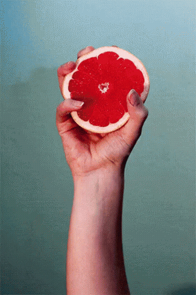 A Woman 'S Hand Is Holding A Slice Of Grapefruit In Her Right Hand GIF
