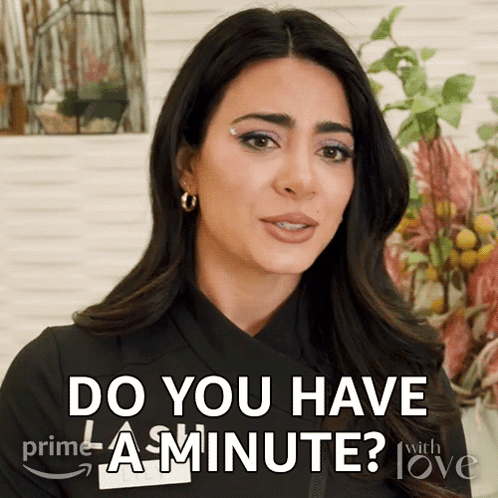 A Woman Says " Do You Have A Minute " In Front Of Flowers GIF