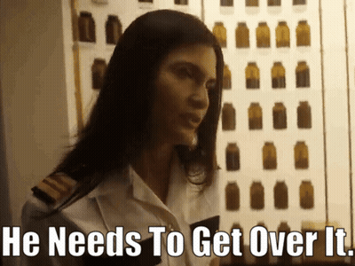 A Woman Says He Needs To Get Over It In Front Of A Wall Of Bottles GIF