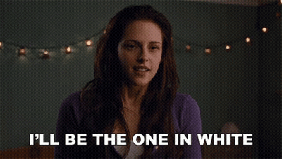 A Woman Says " I 'Ll Be The One In White " In Front Of A String Of Lights GIF
