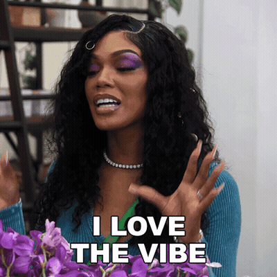 A Woman Says I Love The Vibe In Front Of Some Purple Flowers GIF