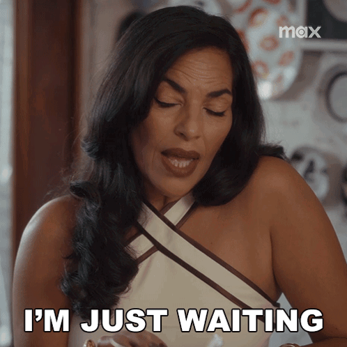 A Woman Says " I 'M Just Waiting " While Sitting At A Table GIF