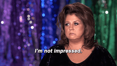 A Woman Says " I 'M Not Impressed " In Front Of Purple And Green Curtain GIF