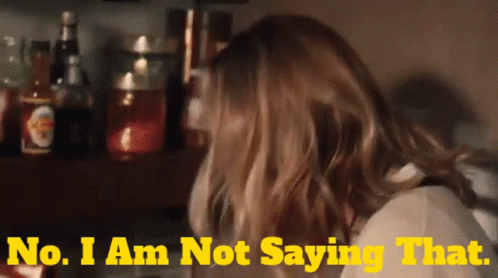 A Woman Says " No I Am Not Saying That " In Front Of A Shelf Full Of Bottles GIF