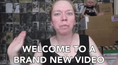 A Woman Says Welcome To A Brand New Video In Front Of Boxes GIF