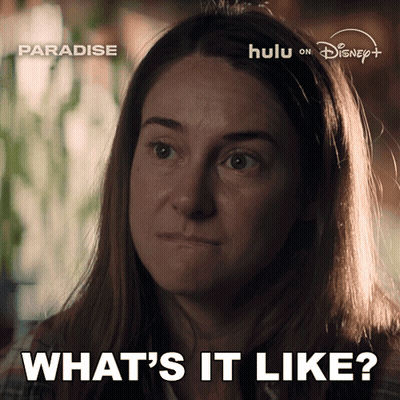 A Woman Says " What 'S It Like " In Front Of A Poster For Paradise GIF