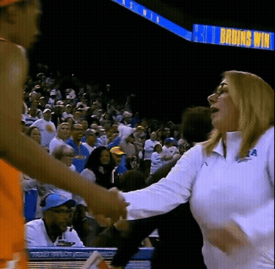 A Woman Shakes Hands With A Basketball Player In Front Of A Sign That Says Bruins Win GIF