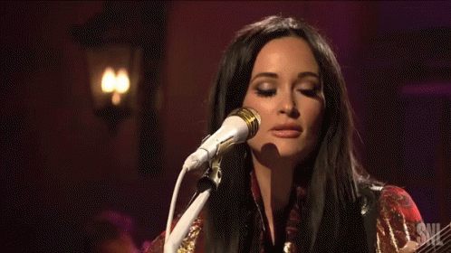 A Woman Singing Into A Microphone And Holding A Guitar GIF