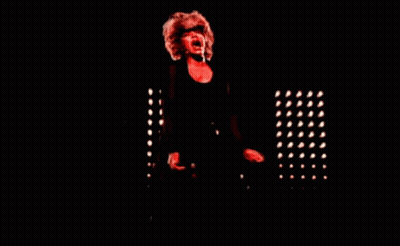 A Woman Singing Into A Microphone In A Dark Room With Red Lights GIF