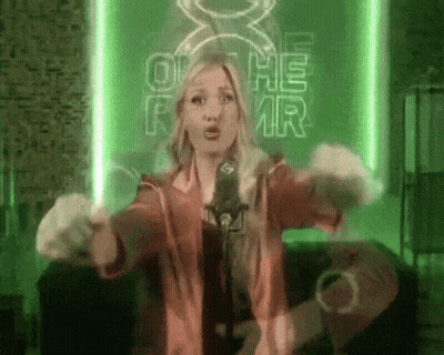 A Woman Singing Into A Microphone In Front Of A Green Sign That Says Oh He Mr. GIF