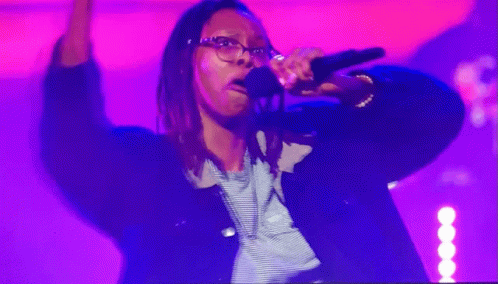 A Woman Singing Into A Microphone In Front Of A Purple Background GIF