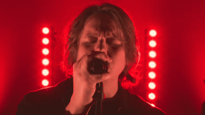A Woman Singing Into A Microphone In Front Of A Red Background GIF