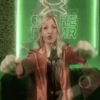 A Woman Singing Into A Microphone In Front Of A Sign That Says O He Rmr GIF