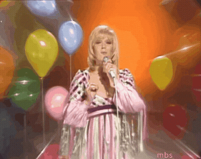 A Woman Singing Into A Microphone In Front Of Balloons With Mbs Written On The Bottom GIF