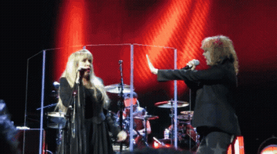 A Woman Singing Into A Microphone Next To A Man GIF