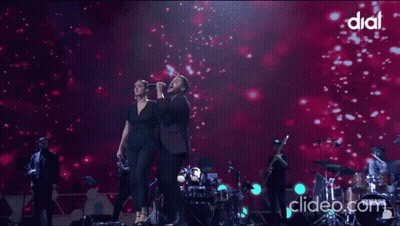 A Woman Singing Into A Microphone Next To A Man On A Stage With Dial Written On The Bottom GIF