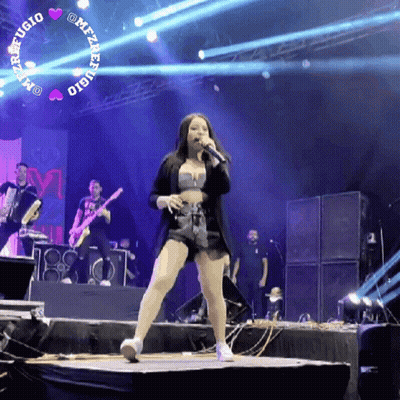A Woman Singing Into A Microphone On Stage With A Band Behind Her GIF