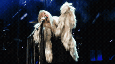 A Woman Singing Into A Microphone Wearing A White Fur Coat GIF