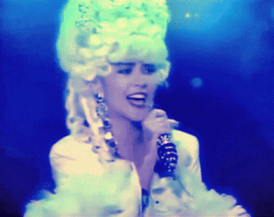 A Woman Singing Into A Microphone Wearing A White Wig GIF