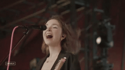 A Woman Singing Into A Microphone While Holding A Guitar In Front Of A Coachella Logo GIF