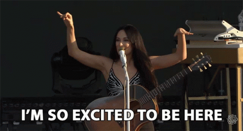 A Woman Singing Into A Microphone While Holding A Guitar With The Words I 'M So Excited To Be Here Below Her GIF
