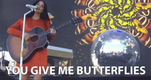 A Woman Singing Into A Microphone While Holding A Guitar With The Words " You Give Me Butterflies " On The Bottom GIF