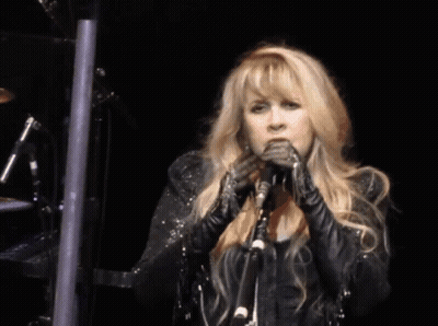 A Woman Singing Into A Microphone While Wearing A Black Jacket GIF
