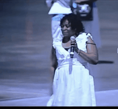 A Woman Singing Into A Microphone While Wearing A White Dress GIF