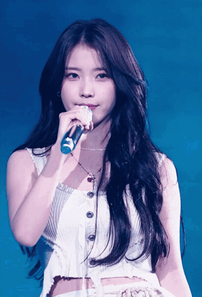 A Woman Singing Into A Microphone While Wearing A White Tank Top GIF