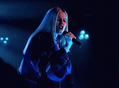 A Woman Singing Into A Microphone With A Blue Background GIF