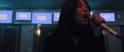 A Woman Singing Into A Microphone With A Blue Screen Behind Her That Says ' Netflix ' On It GIF