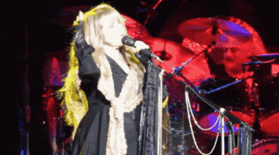 A Woman Singing Into A Microphone With A Drummer Behind Her GIF