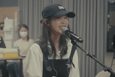 A Woman Singing Into A Microphone With A Ds Hat On GIF