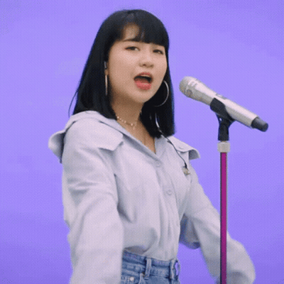 A Woman Singing Into A Microphone With A Purple Background Behind Her GIF