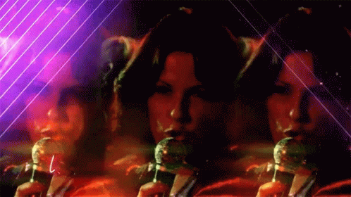 A Woman Singing Into A Microphone With A Purple Background Behind Her GIF