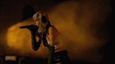 A Woman Singing Into A Microphone With A Sign That Says Campella On The Bottom GIF