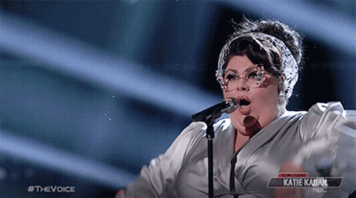 A Woman Singing Into A Microphone With A Sign That Says Katie Kabuk On It GIF
