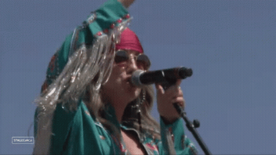 A Woman Singing Into A Microphone With A Sign That Says Stagecoach On It GIF