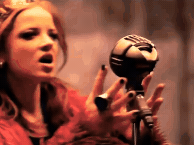 A Woman Singing Into A Microphone With Her Hands GIF