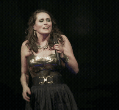 A Woman Singing Into A Microphone With The Words Een Beetje Warm He On The Bottom GIF