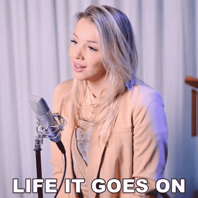 A Woman Singing Into A Microphone With The Words " Life It Goes On " Above Her GIF