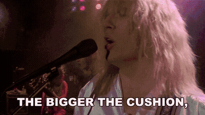 A Woman Singing Into A Microphone With The Words " The Bigger The Cushion " Above Her GIF