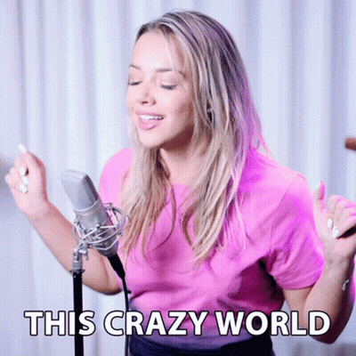 A Woman Singing Into A Microphone With The Words " This Crazy World " Below Her GIF