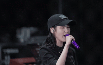 A Woman Singing Into A Purple Microphone Wearing A Baseball Cap GIF