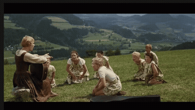 A Woman Singing To A Group Of Children On A Hill GIF