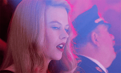A Woman Singing With A Man In A Police Hat In The Background GIF