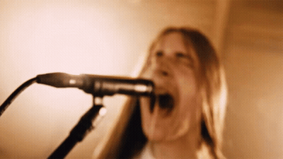 A Woman Sings Into A Microphone With Her Mouth Open GIF