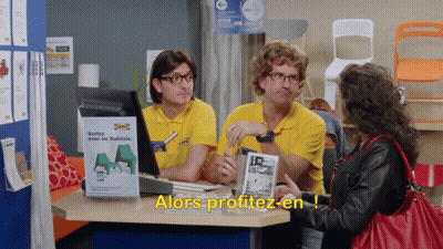 A Woman Sits At A Desk In Front Of A Sign That Says Alors Profitez-En GIF